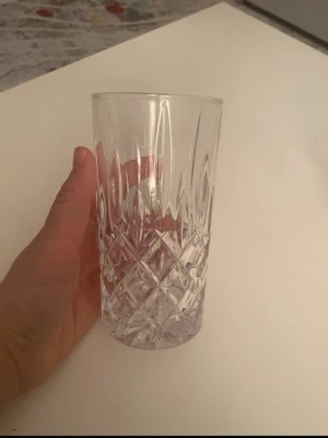 Högt glas med slipat mönster - Säljer ett högt, transparent glas med snyggt slipat rutmönster. Perfekt för kalla drycker och ger en lyxig känsla till dukningen. Glaset har en klassisk form och är tillverkat i klart glasmaterial.