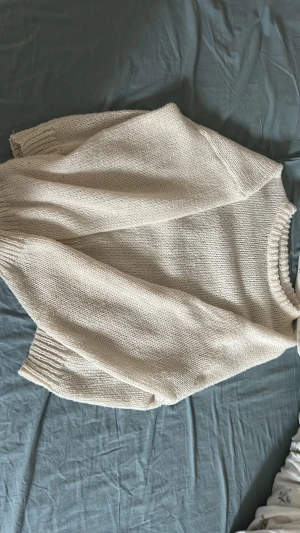 Beige/vit oversized stickad tröja - Mysig beige stickad tröja med oversized passform och breda ribbade muddar vid ärmslut och nederkant. Tröjan har rund halsringning och är gjord i ett mjukt, tjockt garn som passar perfekt för kyligare dagar.