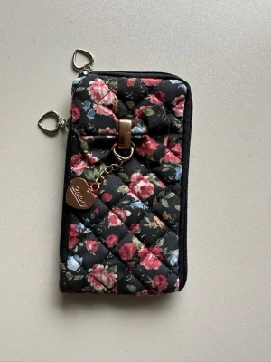 Blommig quiltad plånbok med rosett - Gullig liten portmonnä / plånbok / nyckelväska med dragkedja och extra fack på sidan. 5 x 11 cm. Perfekt för allt krimskrams som man annars måste vända upp och ned på handväskan för att hitta. Mycket fint skick!