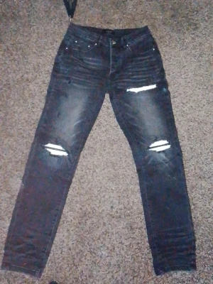 Amiri jeans MX1 size 30 Svarta slitna jeans med hål - Säljer ett par svarta jeans med slitningar och hål vid knäna. Jeansen har en smal passform och klassisk femficksdesign. Perfekta för dig som gillar en edgy och trendig stil. Materialet är denim med stretch för extra komfort.