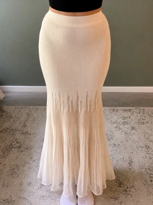Plisserad långkjol i beige - Säljer en elegant plisserad långkjol i cremevit med ribbad midja och lätt utsvängd nederdel. Aldrig använd och prislappen sitter fortfarande kvar.