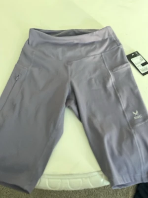 Ljuslila träningsshorts från SOC - Säljer ett par ljuslila träningsshorts från SOC med hög midja och praktiska sidofickor. Shortsen är tillverkade i ett stretchigt syntetmaterial som passar perfekt för aktiva dagar. Diskret logga på ena benet och bekväm passform.