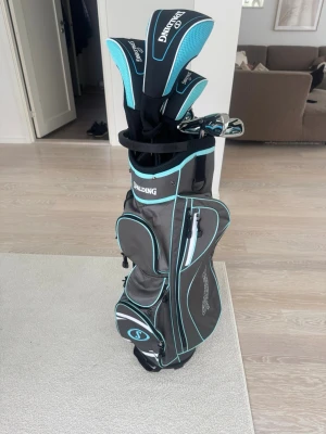 Golfset med bag från Spalding - Snabb viktig info- klubborna är för vänsterhänta och den passar till dam och (ungdom kille)  använd på bana 1 gång och två på ranch. Golfset med flera klubbor och en stilren golfbag från Spalding. Bagen är grå med turkosa och svarta detaljer, har flera fack och bärrem. Klubborna har matchande headcovers i svart och turkos. Perfekt för dig som vill komma igång med golf.
