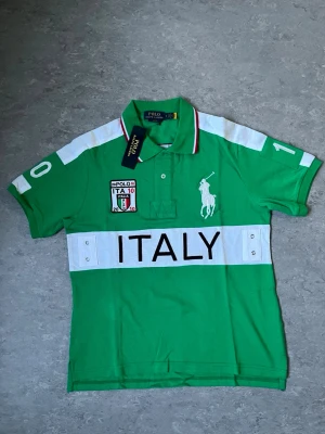 Polo Ralph Lauren Italy piké - Snygg grön pikéskjorta från Polo Ralph Lauren med vit krage och detaljer. Stor broderad logga på bröstet, patch med italiensk flagga och texten ITALY över bröstet. Kortärmad och klassisk pikékrage med knappar.