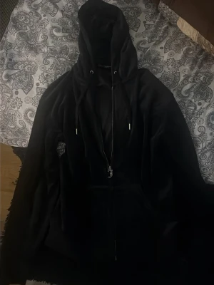 Svart zip hoodie med huva - Säljer en svart hoodie med dragkedja och stor huva. Hoodien har dragsko i huvan och fickor framtill. Materialet ser ut att vara mjukt och bekvämt, perfekt för en chill look. Inga synliga loggor eller tryck.