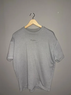 Grå oversized t-shirt New garments  - Snygg grå oversized t-shirt med trycket 'Confidence' och '1998' på ryggen samt liten text på bröstet. T-shirten har rund hals och korta ärmar. Perfekt för en avslappnad och trendig stil.