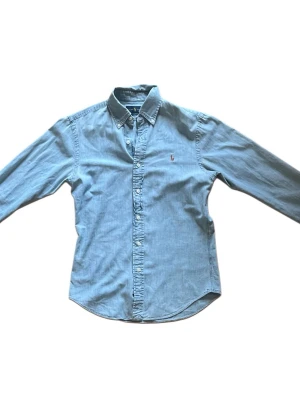 Ljusblå jeans skjorta från Ralph Lauren - Säljer en jeansskjorta från ralph lauren, den sitter s/xs, skjortan är i bra skick, om du har några funderingar är det bara att skriva. Priset är ej hugget i sten