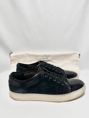 Lanvin Cap Toe Sneakers  - Stilrena svarta sneakers från Lanvin med ovandel i mocka och glansig captoe! Fint skick, inga tydliga defekter. Uk 10, passar 44/45. Dustbag ingår. Kontakta mig för fler frågor och funderingar!