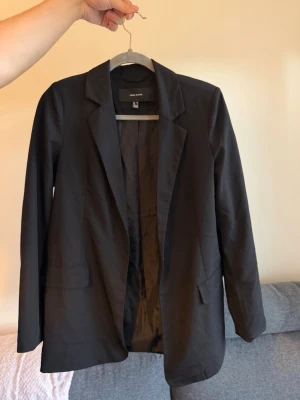 Svart kavaj från Vero Moda - Stilren svart kavaj från Vero Moda med klassisk krage och två framfickor. Rak passform.