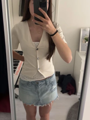 Krämvit v-ringad topp från 157 - Säljer en krämvit v-ringad topp från 157 med korta ärmar och knappar framtill. Toppen har en clean och enkel look som passar perfekt till jeans eller kjol. Materialet känns mjukt och stretchigt, vilket gör den bekväm att bära hela dagen.