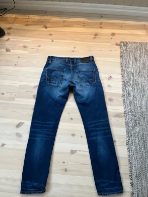 Mörkblå slim fit jeans från Jack and Jones  - Snygga mörkblå slim fit jeans med slitningar och kontrastsömmar. Klassisk femficksmodell med normal midja och raka ben. Perfekta för en avslappnad och trendig look. Materialet är denim i bomull med lite stretch för extra komfort. Från Jack and Jones.