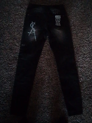 Ksubi jeans size 29 Svarta jeans med tryck - Säljer ett par svarta jeans från 11 by Boris Bidjan Saberi med vita tryckdetaljer, bland annat ett stort dollartecken och texten 'Royalty Heroism And The Streets' på bakfickan. Jeansen har smal passform och är tillverkade i denim.