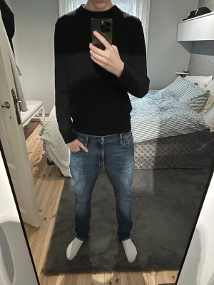 Svart stickad tröja - En enkel svart stickad tröja med rund hals och långa ärmar. Perfekt för lager-på-lager och passar till jeans eller chinos. Materialet är mjukt och stretchigt, vilket gör den bekväm att bära hela dagen.