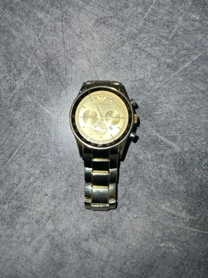 Emporio Armani guld herrklocka - Stilren klocka från Emporio Armani i guldigt metallutförande. Klockan har rund urtavla med flera små visare och klassisk länkarmband. Perfekt accessoar för dig som vill sticka ut med en lyxig look.