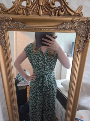 Grön mönstrad jumpsuit med knytband - Snygg grön jumpsuit i storlek S från Mango med vitt grafiskt mönster och knytband i midjan. Köpt second hand och använd någon enstaka gång. Den har några lösa trådar som jag tror att man bara kan klippa bort, men är i övrigt i bra skick. Normal i storlek skulle jag säga, ingen direkt stretch. 