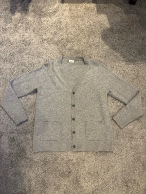 John Henric cardigan - Mysig ljusgrå kofta med v-ringning och fem knappar framtill. Den är gjord av 100% cashmere vilket är ett eftertraktat material. Den passar även till det mesta. Hör av dig vid minsta fundering!