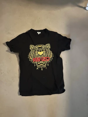 Kenzo t-shirt - Svart kenzo t-shirt med guld och rött, i storlek S. Skicket är bra, industrie tag är korrekt. Köpt i Las Vegas, säljs för ca. 1700kr begagnad. 