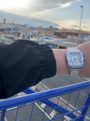 En fin klocka köpte den utomlands  - Säljer en stilren klocka i silverfärgat stål med kvadratisk boett och klassisk vit urtavla med romerska siffror. Klockan har blå visare och datumfönster vid sexan. Länkarmband i borstat och polerat stål för en lyxig känsla.