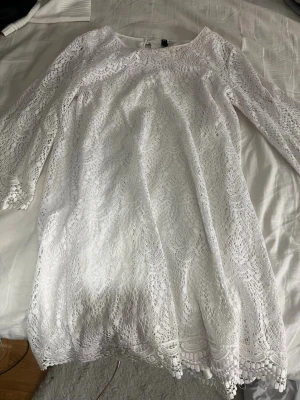 Vit spetsklänning med trekvartsärm - Söt vit klänning i spets med trekvartsärm och rund hals. Klänningen har fina spetsdetaljer och dekorativ kant längst ner samt vid ärmsluten. Perfekt för sommarens alla tillfällen.