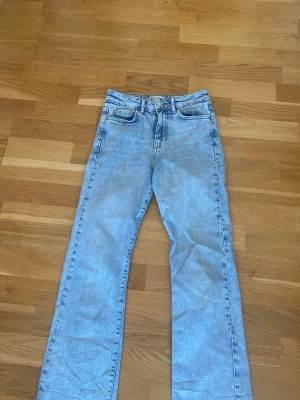 Ljusblåa raka jeans  - Säljer ett par ljusblå jeans med rak passform och hög midja. Jeansen har fem fickor och rå, fransig kant längst ner på benen för en avslappnad look. Tillverkade i klassisk denim med en cool vintagekänsla. Två små fläckar som inte syns när man har på sig jeansen!! Se bild 5 och 6.