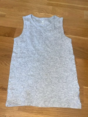 Ljusgrå ärmlös linnetopp H&M - En enkel och mjuk ljusgrå linnetopp från H&M Basic i ekologisk bomull. Toppen är ärmlös med rund halsringning och har en clean, minimalistisk look som passar till allt. Perfekt för lager på lager eller sommarens varma dagar. Några små fläckar men som knappt syns!!