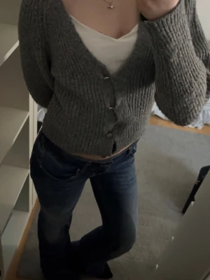 Grå stickad kofta från Only - Säljer en mysig grå stickad kofta från Only med v-ringning och knappar framtill. Perfekt för kyliga dagar med sin ribbade design och långa ärmar. En stilren och bekväm tröja för alla tillfällen. Storleken är lik XS förutom lite kortare ärmar.