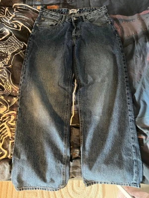 Baggy blå jeans från 157 - Säljer ett par baggy blå jeans från 157 med bred passform och raka ben. Klassisk femficksmodell i slitstark denim med knappgylf och bälteshällor. Perfekta för en avslappnad och trendig look. Storlek 38/short