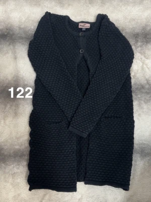 Svart lång kofta från Pomp de Lux - Mysig lång kofta i svart från Pomp de Lux med strukturerad stickning och två knappar framtill. Koftan har långa ärmar och två fickor framtill, perfekt för lager-på-lager-stil.🌸Fint använt skick. Har två knappar längst upp. Storlek 122 