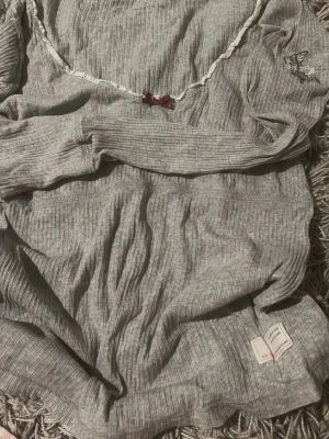 Grå ribbad topp Odd Molly - Supersöt grå ribbad topp från Odd Molly med liten rosett framtill och spetskant vid urringningen. Toppen har en diskret fågel ”brodyr”  på axeln och är gjord i mjukt material som känns skönt mot huden. Perfekt för en chill och avslappnad look.