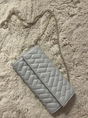 Ljusgrå quiltad kuvertväska - Snygg ljusgrå kuvertväska med quiltat mönster och guldfärgad kedja. Väskan har en stilren rektangulär form och stängs med lock. Perfekt accessoar för att lyfta din outfit med en trendig touch. Används inte längre💞💞