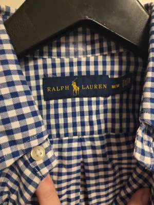 Rutig skjorta från Ralph Lauren M - Säljer två klassiska rutiga skjortor från Ralph Lauren i storlek M. Ena är blåvit och den andra rödvit, båda med knappar framtill och broderad logga på bröstet. Skjortorna har lång ärm och är gjorda i mjuk bomull som känns skön mot huden.