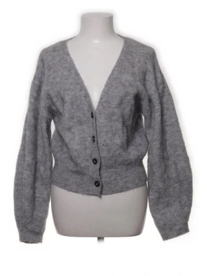 Grå stickad kofta med knappar - Mysig grå stickad kofta med v-ringning och fyra svarta knappar framtill. Koftan har långa, lite puffiga ärmar och ribbstickade muddar vid ärmslut och nederkant. Perfekt för lager-på-lager och chill dagar.