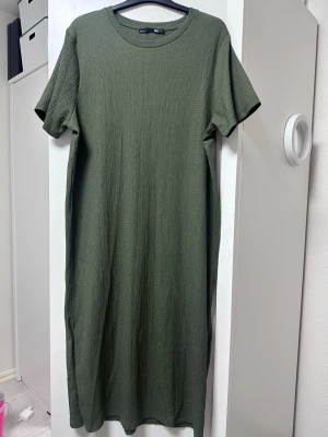 Olivgrön  t-shirtklänning - En enkel och stilren olivgrön t-shirtklänning. Klänningen har korta ärmar, rund halsringning och är tillverkad i ett ribbat bomullstyg som ger en avslappnad känsla. Perfekt för en chill och bekväm look.