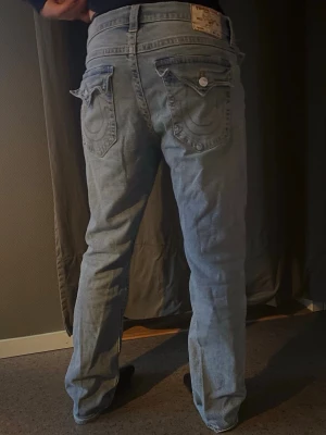 Ljusblå True Religion jeans - Säljer ett par ljusblå jeans från True Religion med klassiska kontrastsömmar och snygga fickdetaljer bak. Jeansen har rak passform och är tillverkade i denim med en lätt tvättad look. Perfekta för dig som gillar streetwear och vill sticka ut lite extra.