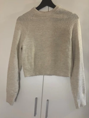 Beige cropped stickad tröja  - Säljer en beige cropped stickad tröja från hm då den inte kommer till användning. Använt få antal gånger. Tröjan har rund halsringning, långa ärmar och ribbstickade muddar vid ärmslut och nederkant. Perfekt för lager-på-lager och enkel att matcha med jeans eller kjol.💕