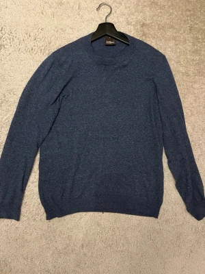 Blå stickad tröja från Oscar Jacobson - Mörkblå stickad tröja från Oscar Jacobson, tillverkad i Italien. Tröjan har rund halsringning, långa ärmar och en klassisk, stilren design. Perfekt för dig som gillar enkel och snygg stil.