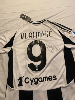 Juventus matchtröja Vlahović #9 - Juventus officiella matchtröja i svart och vitt med Vlahović och nummer 9 på ryggen. Tröjan har Adidas-logga, Juventus klubbmärke, sponsortryck samt autograf. Tillverkad i Italien och tröjan är äkta och jag vann den på fotbollskanalens tävling slide 4 som bevis. Priset kan sänkas vid snabb affär till ett rimligt pris