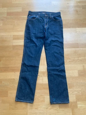 Blå slim fit Jeans från nudie - Säljer ett par mörkblå slim Jim jeans från Nudie Jeans med klassisk femficksmodell och kontrastsömmar. Hör av dig vid minsta lilla fråga. Skick 9,6/10 W33 L34