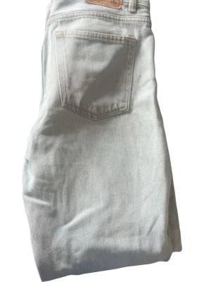Ljusblå jeans med klassisk passform - Säljer ett par ljusblå jeans med klassisk femficksdesign och raka ben. Jeansen har en snygg bakficka och ett läderpatch vid linningen. Perfekta för dig som gillar en enkel och stilren look. Materialet är denim.