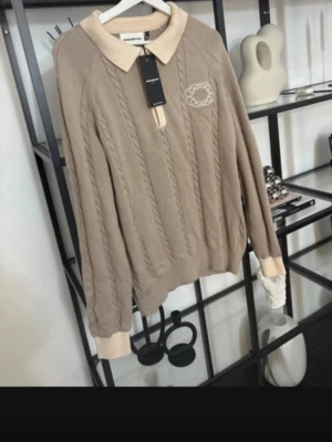 Beige kabelstickad tröja Prohibited - Snygg beige kabelstickad tröja från Prohibited med krage i kontrasterande ljusbeige. Tröjan har ett broderat logotypmärke på bröstet och ribbade muddar. Perfekt för dig som gillar klassisk men trendig stil.