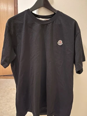 Svart Moncler t-shirt med logga - Snygg svart t-shirt från Moncler med klassisk rund hals och liten Moncler-logga på bröstet. Tillverkad i mjuk bomull och har en enkel, stilren design som passar perfekt till jeans eller shorts.