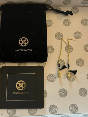 Guldpläterade örhängen  - Snygga Guldpläterade örhängen från Daily Elegance med tunna kedjor, svarta pärlor och små svarta tofsar. Örhängena har en elegant och modern design som sticker ut. Perfekta för dig som gillar unika accessoarer.