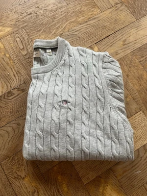 Kabelstickad GANT - Ljusgrå kabelstickad tröja från GANT. Klassisk modell som passar till det mesta. Tröjan är helt oanvänd och i nyskick, utan hål eller fläckar. Mjuk och bekväm kvalitet. Nypris ca 1099🙌