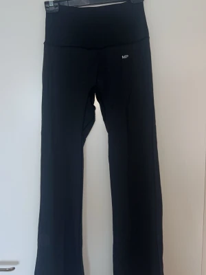 Svarta bootcut leggings/träningsbyxor  från MP - Säljer ett par svarta leggings/träningsbyxor  från MP med bootcut-ben och hög midja. De har en enkel design utan synliga fickor och är tillverkade i ett stretchigt material som sitter skönt på kroppen.
