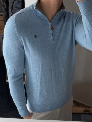 Ljusblå halvzip-tröja Morris - Ljusblå stickad tröja från Morris med halv dragkedja och ribbade muddar. Tröjan har en liten broderad logga på bröstet och är tillverkad i mjukt material som passar perfekt till en avslappnad men stilren look. Storlek m men har krympt så sitter som xs 