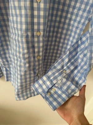 Blårutig skjorta från Banana Republic - Snygg blårutig skjorta från Banana Republic i bomull. Skjortan har klassisk krage, långa ärmar med manschett och vita knappar framtill. Perfekt för en clean och fräsch stil.Rutig skjorta i bomull