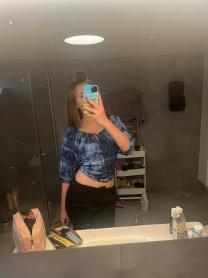 Blå croppad blus med knyt - Säljer en blå croppad blus med knyt framtill och trekvartsärmar. Blusen har ett coolt mönster som liknar batik och är perfekt för dig som gillar en avslappnad och trendig stil. Materialet känns lätt och bekvämt. Blir perfekt till sommaren.