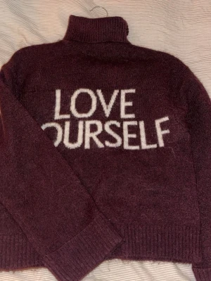Vinröd polotröja med text - Mysig vinröd stickad polotröja med vit text 'LOVE YOURSELF' framtill. Tröjan har långa ärmar, ribbstickade muddar och hög krage. Perfekt för kalla dagar och som aldrig har kommit till användning❤️