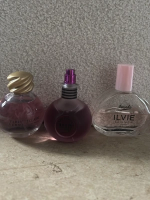 Tre olika damparfymer mixade flaskor - Säljer tre snygga damparfymer: Fabio Verso Eclaire i rund flaska med guldlock, Ilvie Eau de Parfum i genomskinlig flaska med rosa lock och en lila parfym med metalliskt sprayhuvud ( Katy Perry Mad portion). Alla flaskor har unik design och passar perfekt i badrumshyllan.💕💕 alla tre säljs ihop för priset 🩷🩷🤩