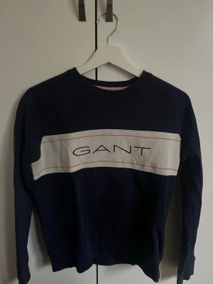 Mörkblå sweatshirt från GANT - Snygg mörkblå sweatshirt från GANT med vit panel och logga framtill. Tröjan har rund halsringning och långa ärmar. Perfekt för en avslappnad och stilren look. Tillverkad i mjukt material för extra komfort.
